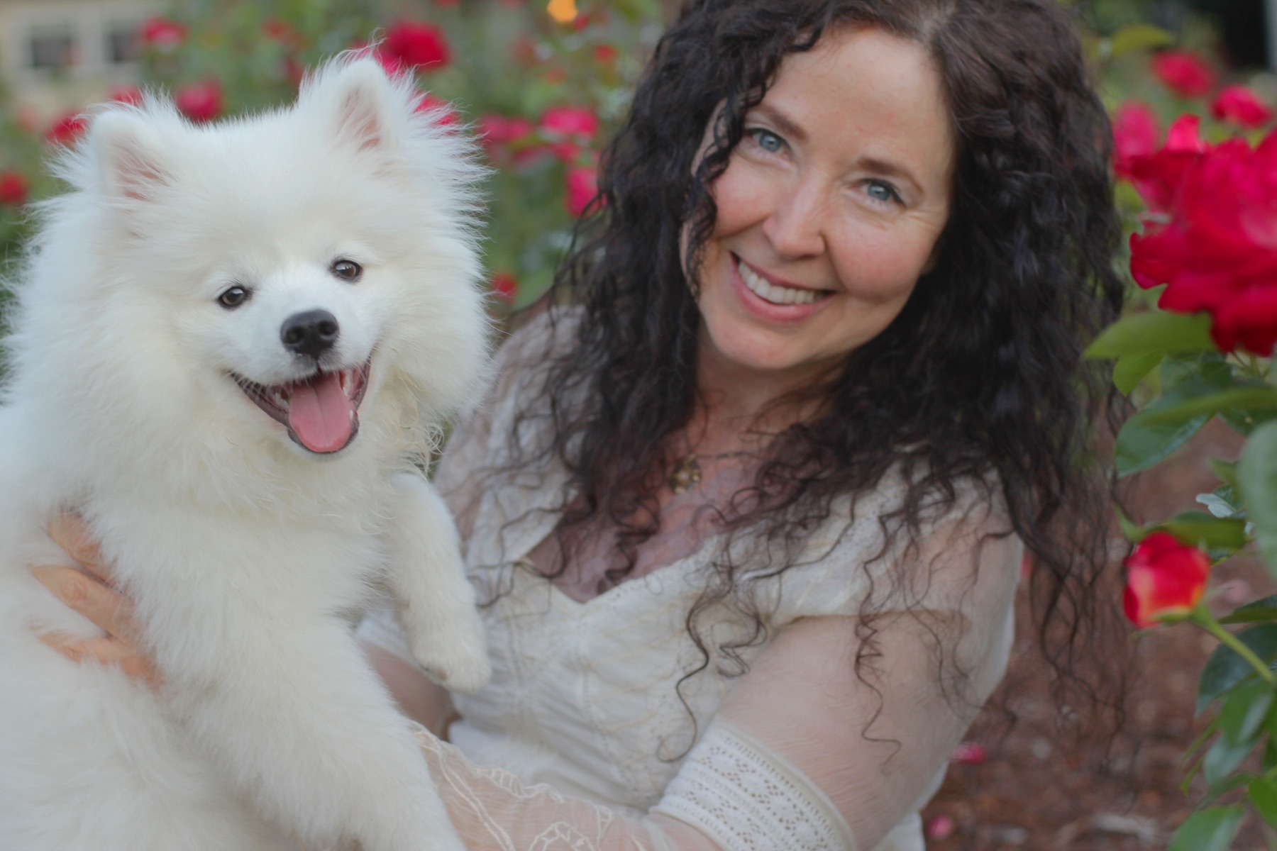 Susan Hiera Bass holding her dog Halo in a red rose garden